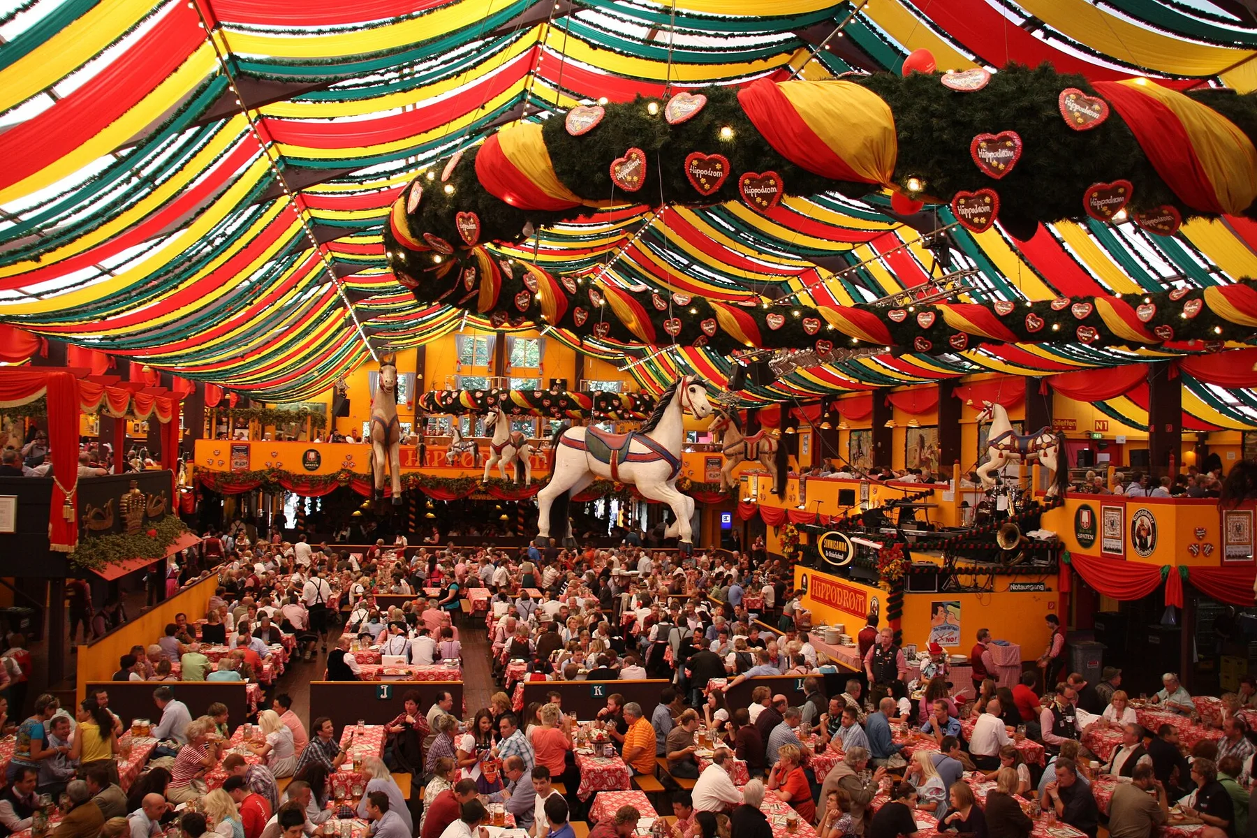 Large Oktoberfest tent decorated with colorful fabric, greenery, lights and hanging gingerbread hearts