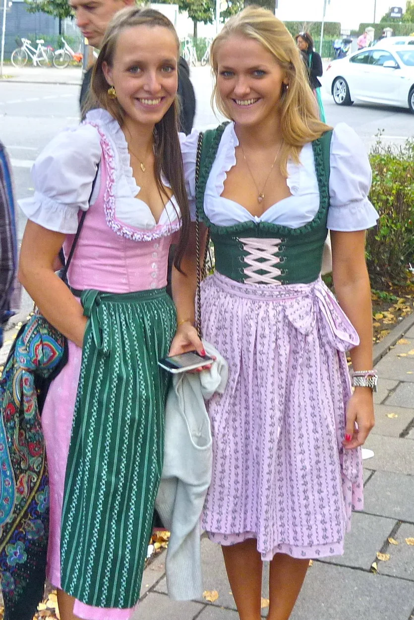 Two Oktoberfest visitors wearing midi dirndls with fitted bodices, white blouses and tied aprons