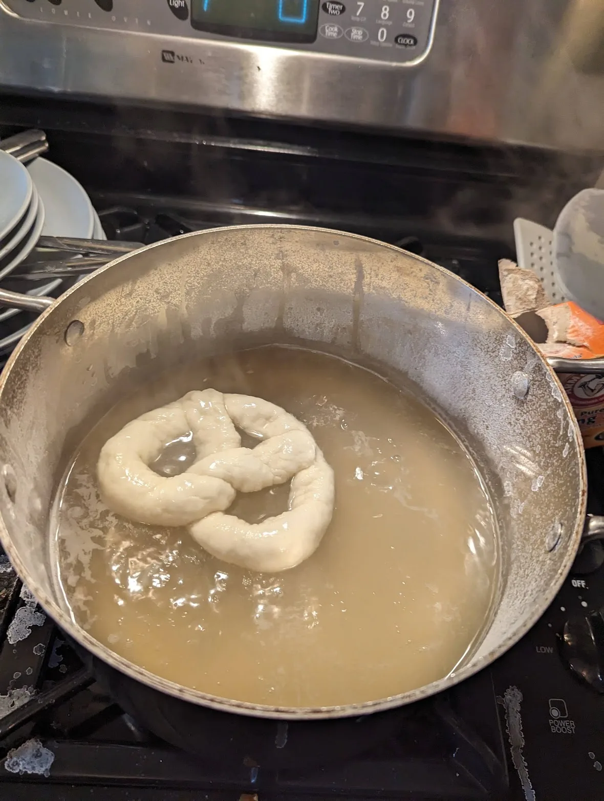 Shaped pretzel dough simmering in a pot of baking-soda water