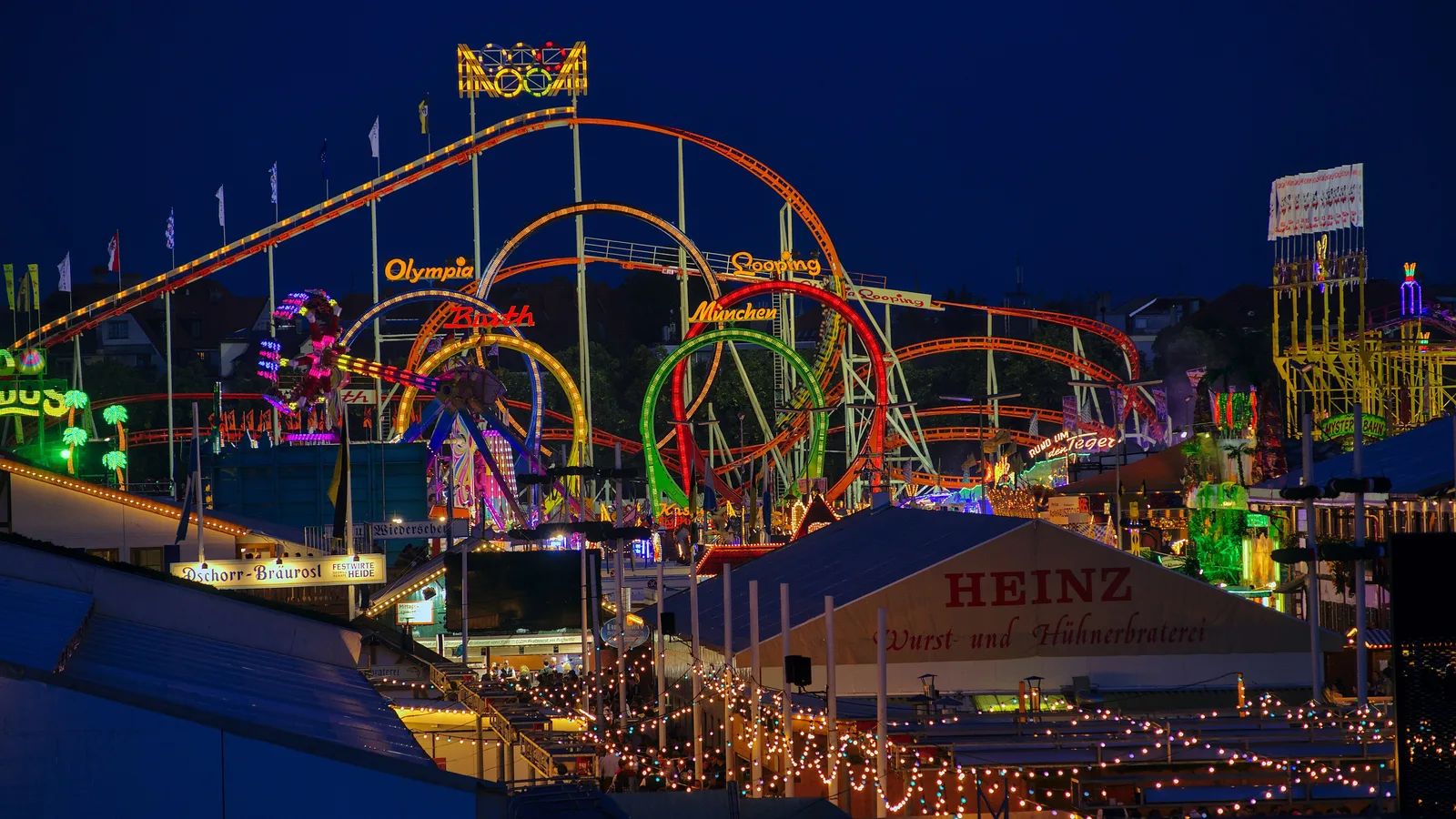 Illuminated roller coasters and festival tents across the Munich Oktoberfest grounds at dusk