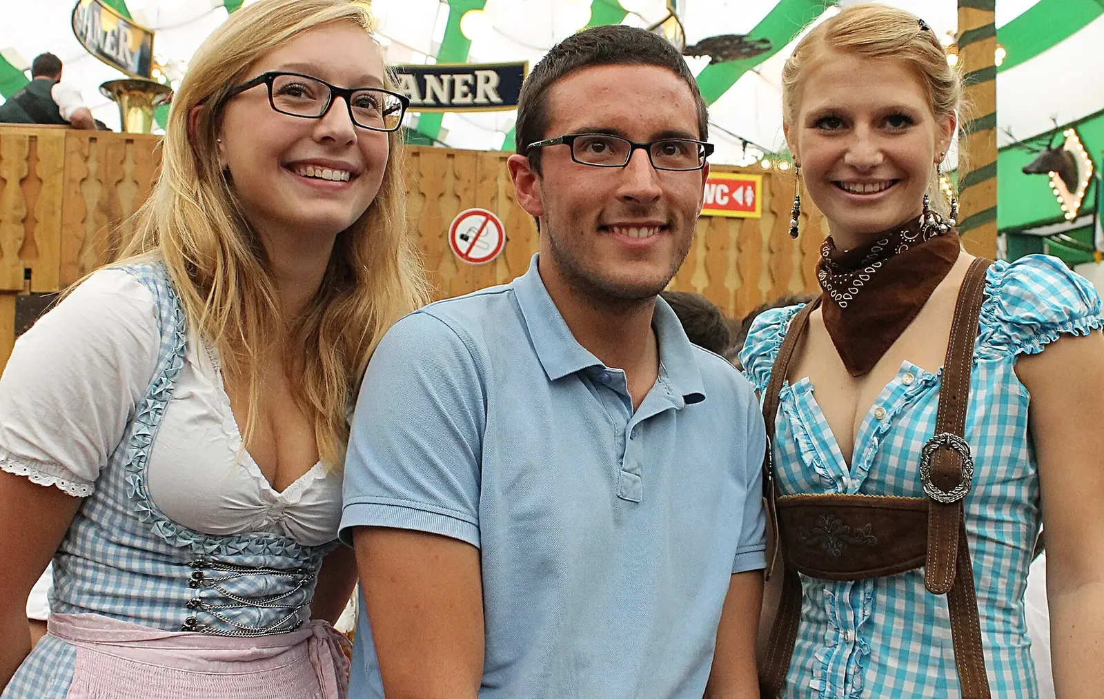 Oktoberfest visitors wearing dirndls alongside a guest in a casual polo shirt